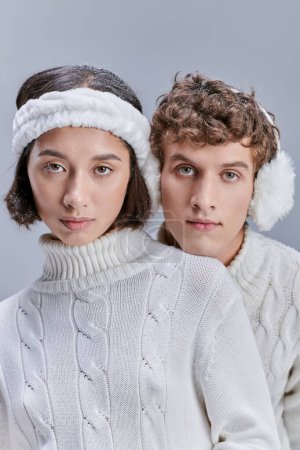 young interracial models in warm cozy clothes looking at camera on grey, winter fashion campaign