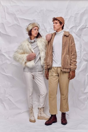 young interracial couple in stylish winter outfit on white textured background, urban fashion