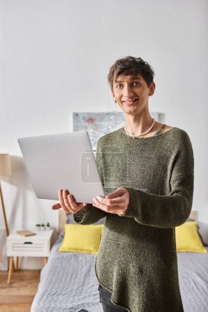 blogger transgénero con cabello rizado usando laptop mientras está de pie en apartamento moderno, influencer