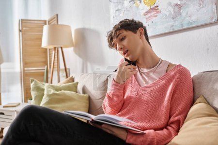 Transgender-Freelancer im rosafarbenen Pullover spricht auf dem Smartphone und schreibt zu Hause in Notizbuch