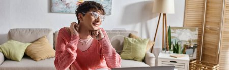 happy transgender freelancer in pink sweater and glasses looking away at home, horizontal banner