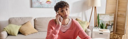 curly androgynous freelancer in pink sweater and eyeglasses talking on smartphone, banner