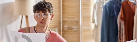 curly androgynous freelancer in pink sweater and eyeglasses working remotely, paperwork banner