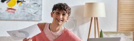 happy androgynous freelancer in pink sweater and eyeglasses working remotely, paperwork banner