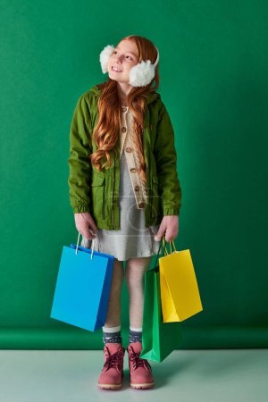 Black Friday und Ferienzeit, verträumtes Mädchen im Winteroutfit und Ohrenschützer mit Einkaufstaschen
