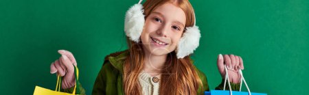 holiday season banner, happy preteen girl in winter outfit and ear muffs holding shopping bags