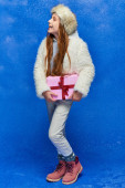 winter joy, happy preteen girl in faux fur jacket and hat holding gift box on turquoise background Tank Top #680994720