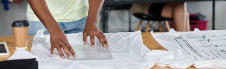 cropped view of african american designer holding plastic format template near white t-shirt, banner