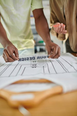 cropped view of interracial fashion designers holding text templates near t-shirt with format sizes