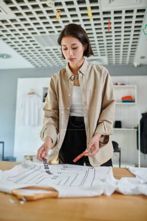 young female asian designer holding text template near clothing with format sizes in print studio