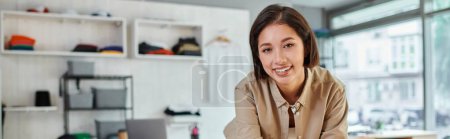 junge erfolgreiche asiatische Modedesignerin lächelt in moderner Druckerei in die Kamera, horizontales Banner