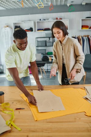 Foto de Diseñadores de ropa multiculturales creativos que trabajan con patrones de costura en un estudio de impresión moderno - Imagen libre de derechos