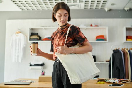 successful asian designer with canvas shopping bag and coffee to go in modern print studio