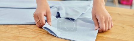 Ausgeschnittene Ansicht einer fleißigen Frau, die in einer Textildruckerei arbeitet, während sie Kleidung faltet, Banner