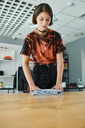 jeune et élégant asiatique femme pliage vêtements soigneusement dans textile imprimer studio, petite entreprise