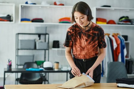 heureux asiatique femme emballage soigneusement plié vêtements sur la table dans textile imprimer studio, industrie de la mode
