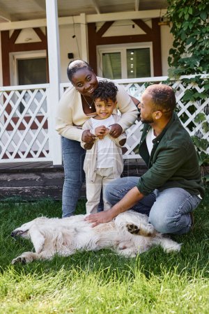 Foto de Padres afroamericanos alegres e hijo jugando con el perro en el patio trasero de su casa, tiempo de calidad - Imagen libre de derechos