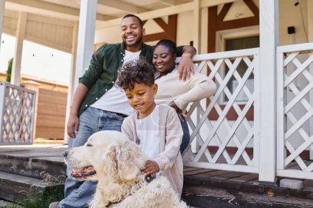 positive african american kid playing with dog near parents on backyard of their house, quality time