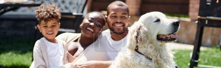 Familienbanner fröhlicher afrikanisch-amerikanischer Eltern und Sohn lächelnd auf Rasen neben Hund sitzend