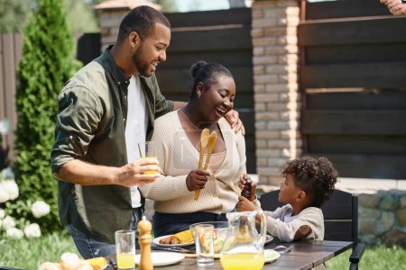 Porträt glücklicher afrikanisch-amerikanischer Eltern und ihres Sohnes beim Zubereiten des Mittagstisches im Garten im Hinterhof