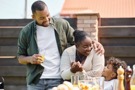 retrato de los padres afro-americanos felices y el hijo teniendo partido de barbacoa de la familia en el patio trasero del hogar