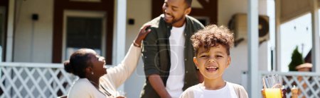 happy african american boy holding glass of orange juice near parents on backyard, banner