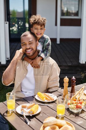 glücklich afrikanisch-amerikanisches Kind umarmt Vater beim Grillen im Hinterhof des Hauses, Familie