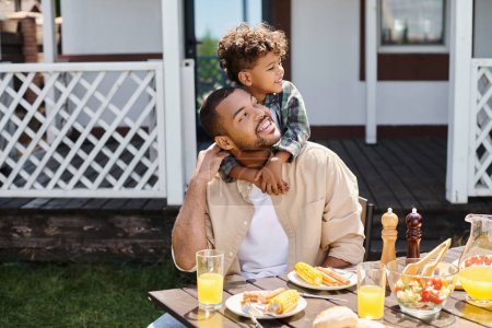 fröhliche afrikanisch-amerikanische Kind umarmt Vater beim Grillen im Hinterhof des Hauses, Familie