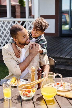 niño afroamericano positivo abrazando al padre excitado en aparatos ortopédicos en el patio trasero de la casa, tiempo en familia