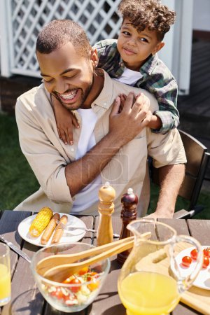 niño afroamericano sonriente abrazando al padre emocionado en aparatos ortopédicos en el patio trasero de la casa, tiempo en familia