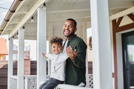 happy moments, joyful african american boy sitting on porch and holding hands with father in braces