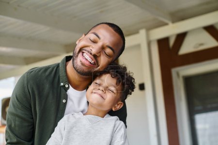 joyful african american boy and cheerful father smiling with closed eyes while having good time