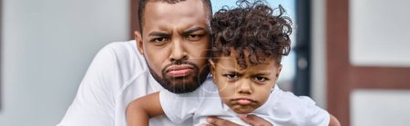 funny portrait of african american son and father looking displeased and looking at camera, banner