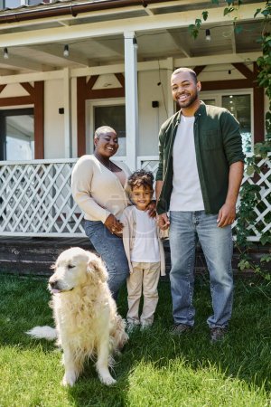 Foto de Foto familiar, padres afroamericanos alegres e hijo sonriendo cerca lindo perro en el patio trasero de la casa - Imagen libre de derechos