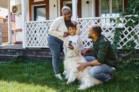 Foto de Foto familiar, padres afroamericanos felices e hijo sonriendo cerca de lindo perro en el patio trasero de la casa - Imagen libre de derechos