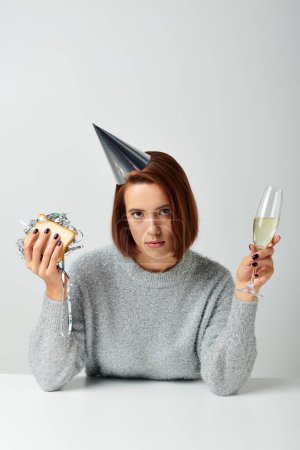 junge Frau in Partymütze hält Sandwich mit Lametta und Champagnerglas in der Hand und feiert Neujahr