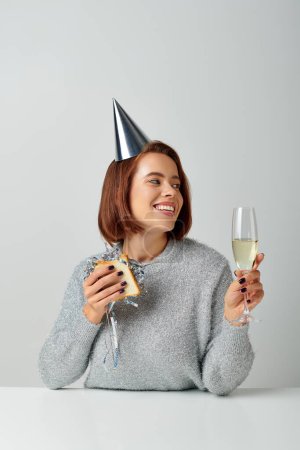 glückliche Frau mit Partymütze, Sandwich mit Lametta und Champagnerglas in der Hand, feiert Neujahr