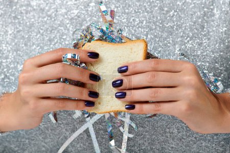 Nahaufnahme einer beschnittenen Frau, die ein Sandwich mit Lametta auf grauem Hintergrund hält, Happy New Year Konzept