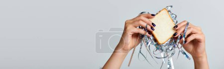 partial view of woman holding sandwich with tinsel on grey backdrop, Happy New Year concept, banner