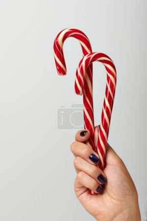 vista recortada de la mujer sosteniendo espiral bastones de caramelo rojo sobre fondo gris, concepto de Feliz Navidad