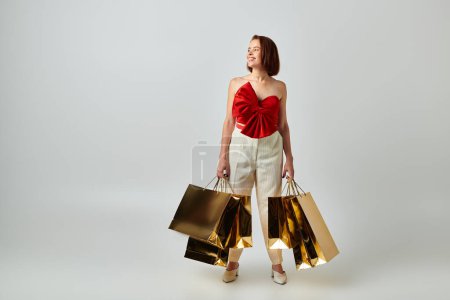 Foto de Compras de vacaciones, mujer feliz en traje de moda sosteniendo bolsas de compras sobre fondo gris, Navidad - Imagen libre de derechos