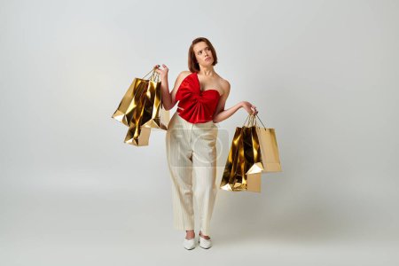 holiday shopping, confused woman in stylish attire holding shopping bags on grey background