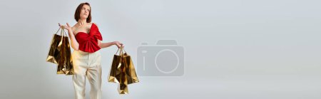holiday shopping banner, pensive woman in stylish attire holding shopping bags on grey background