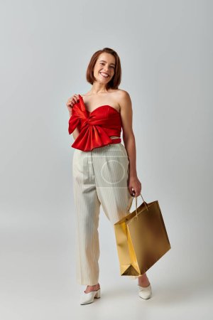 Weihnachtseinkäufe, fröhliche junge Frau in trendiger Kleidung mit Einkaufstasche auf grauem Hintergrund