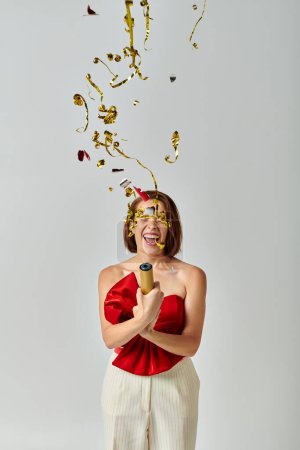 Foto de Feliz Año Nuevo, mujer joven emocionada en traje de moda aplaudiendo confeti festivo sobre fondo gris - Imagen libre de derechos