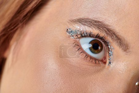 Nahaufnahme einer jungen Frau mit Urlaubs-Make-up, einem weiblichen Auge mit schimmerndem Lidschatten, das wegschaut