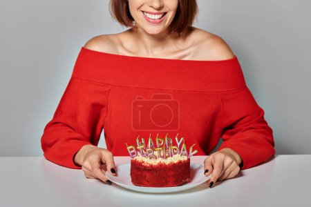 brünette Frau in roter Kleidung mit einem Stück Bento-Kuchen auf grauem Hintergrund, Happy Birthday
