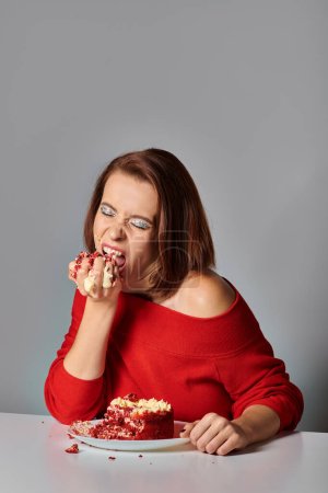 cumpleañera hambrienta con los ojos cerrados comiendo delicioso pedazo de pastel de terciopelo rojo sobre fondo gris