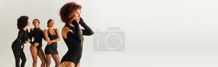 Photo for Appealing sexy african american women in black stylish bodysuits posing together, fashion, banner - Royalty Free Image