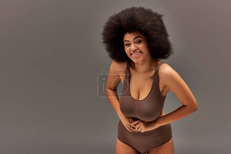 modelo femenino afroamericano alegre en ropa interior pastel sonriendo felizmente, concepto de moda